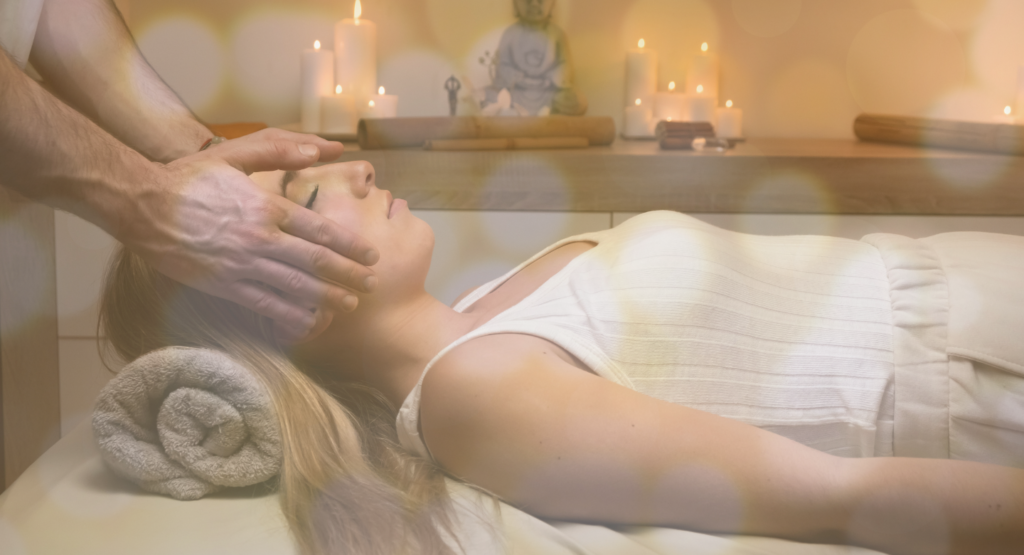 women lying on massage table getting reiki on head with candles in the background